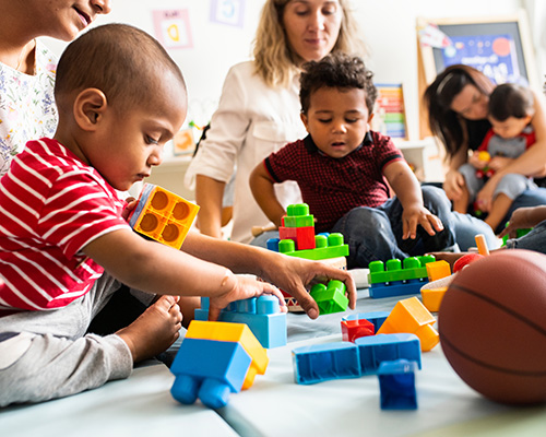 Diverse children and their female teachers playing with building blocks in an early childhood classroom.