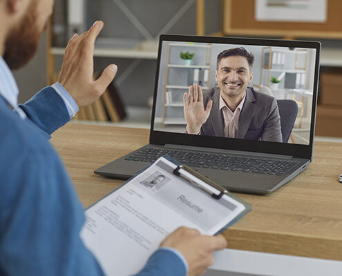 A hiring manager in his home office greets an interviewee on the computer for their virtual interview.