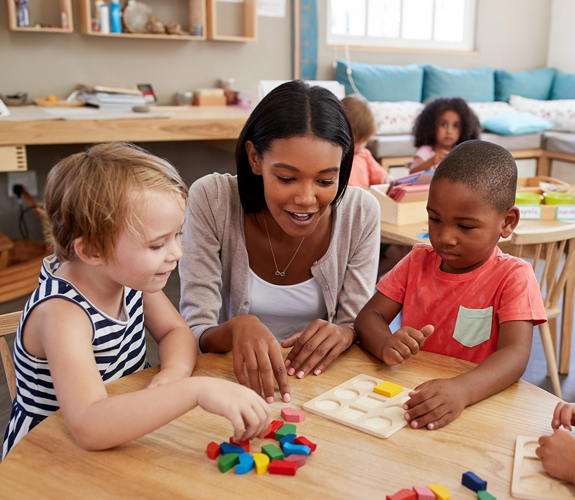 A preschool teacher works with young children on a block puzzle.