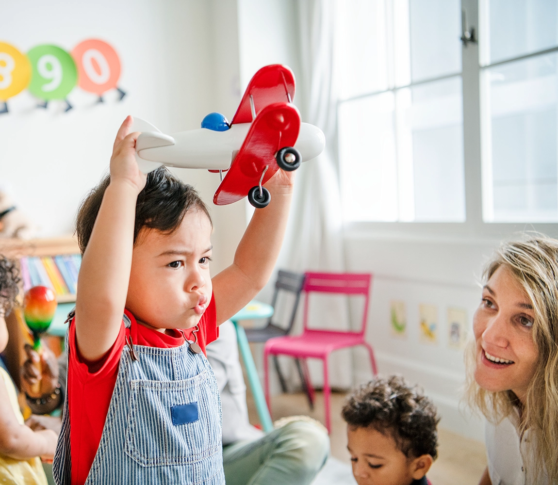 A young child zooms an airplane toy around a toddler classroom.